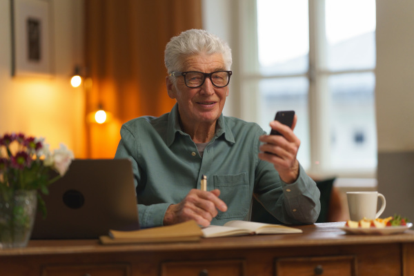 Senior man writing notes in his diary, with opened computer.