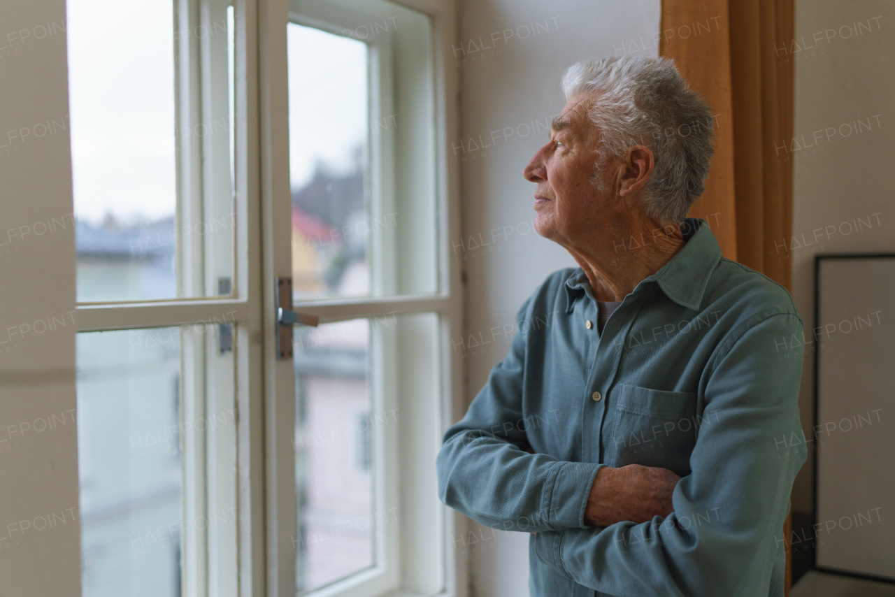 Senior man looking out of a window, concept of solitude in retirement.