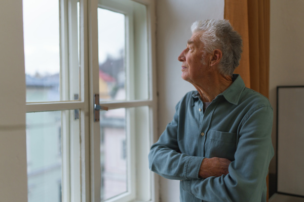 Senior man looking out of a window, concept of solitude in retirement.