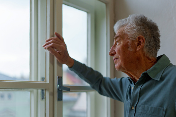 Senior man looking out of a window, concept of solitude in retirement.