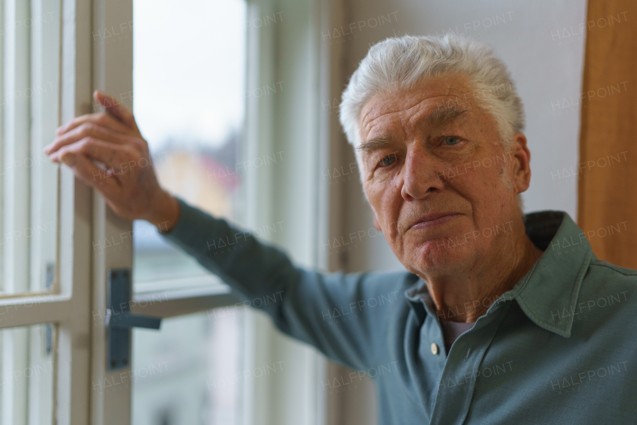 Senior man standying near the window, concept of solitude in retirement.