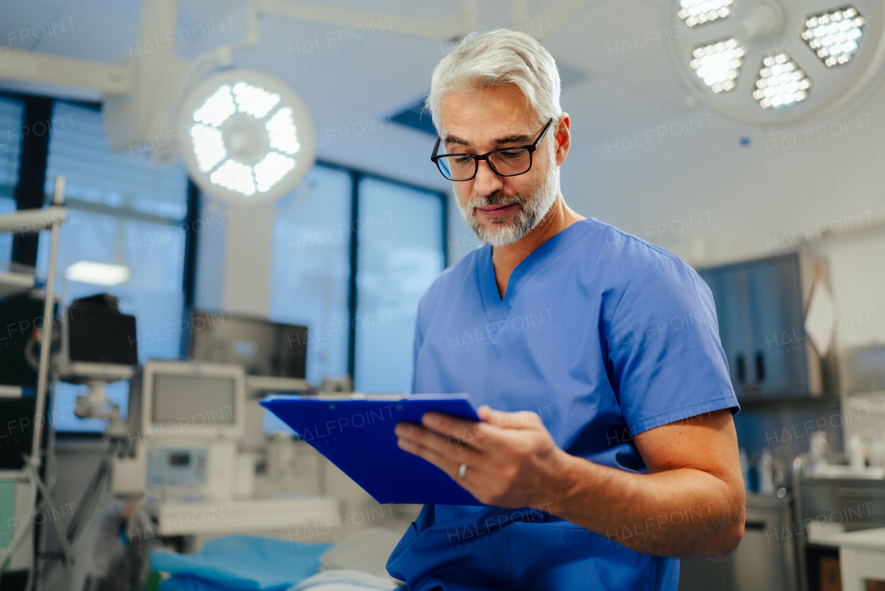 Portrait of handsome male doctor in scrubs. ER doctor examining patient, reading medical test, lab results in clipboard. ER with patient with life threatening health problems.