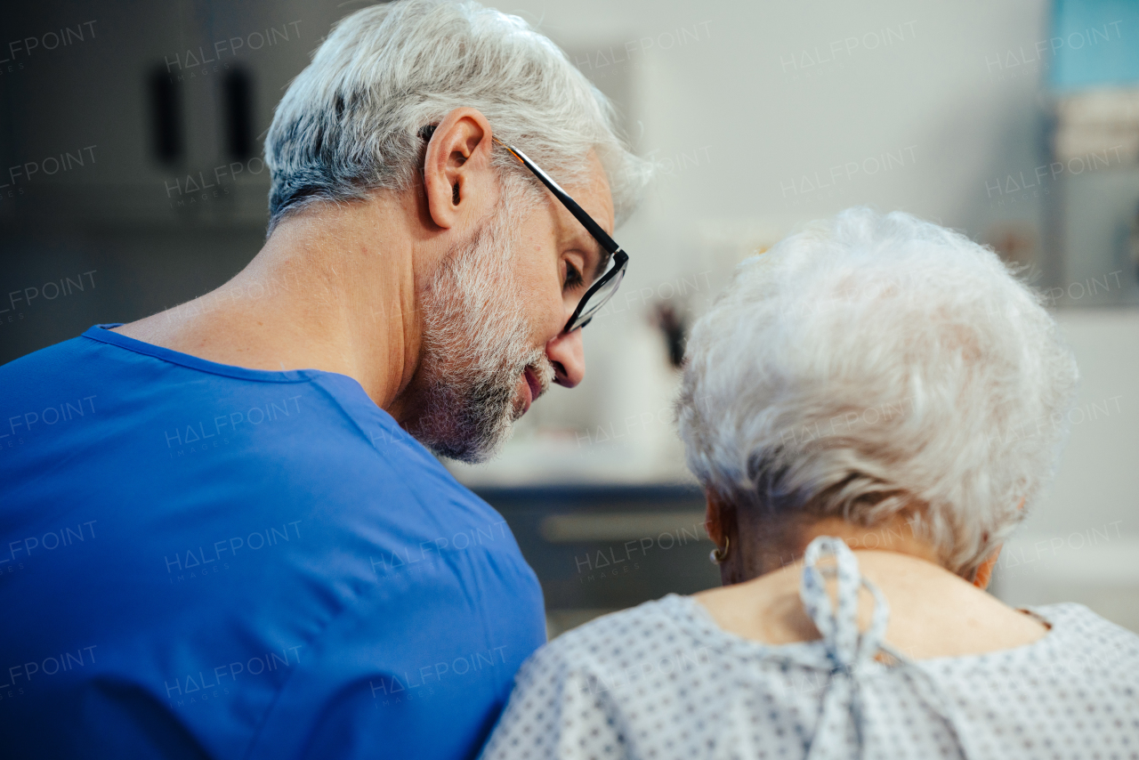 Supportive doctor soothing a worried senior patient, discussing test result in emergency room. Compassionate emotional support for elderly patient.