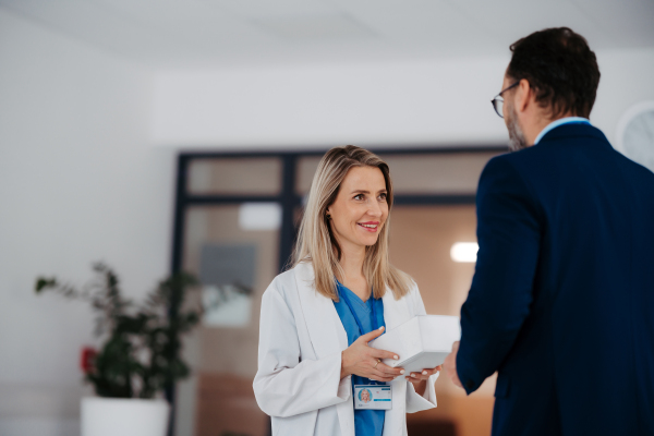 Pharmaceutical sales representative talking with the female doctor in medical building convicing her to try new pharmaceutical product. Doctor holding box with drug samples.