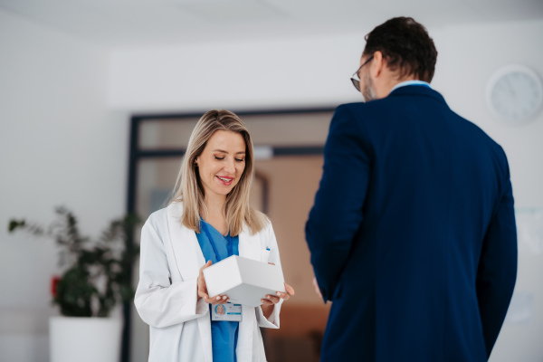 Pharmaceutical sales representative talking with the female doctor in medical building convicing her to try new pharmaceutical product. Doctor holding box with drug samples.