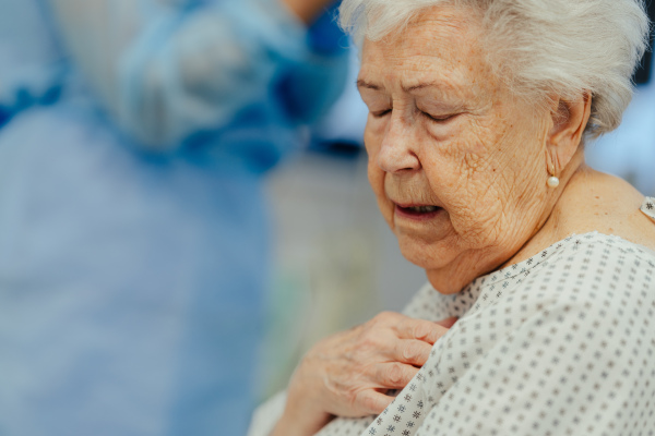 Senior woman after stroke, heart attack feeling chest pain. Elderly patient in hospital gown in emergency room waiting for examination.