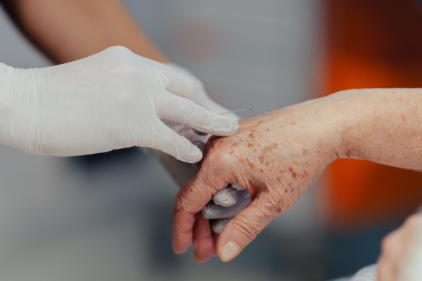 Close up of nurse insering IV cannula in vein, hand. Senior woman in intensive care unit in hospital. IV, intravenous therapy for elderly female patient.