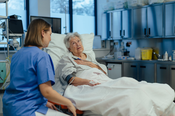 Nurse taking care of senior patient in intensive unit care, icu. Senior woman after stroke, heart attack recoverying, lying in hospital bed.