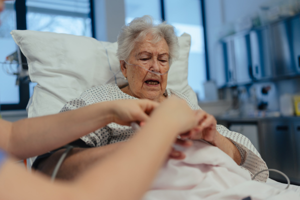 Nurse taking care of senior patient in intensive unit care, icu. Senior woman after stroke, heart attack recoverying, lying in hospital bed.