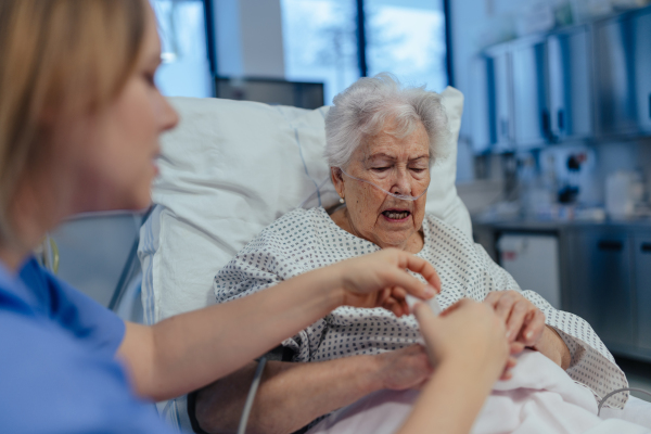 Nurse taking care of senior patient in intensive unit care, icu. Senior woman after stroke, heart attack recoverying, lying in hospital bed.