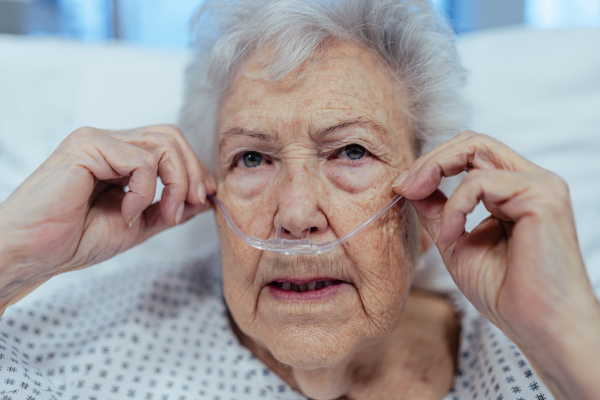 Portrait of senior woman after stroke, heart attack recoverying, lying in hospital bed. Elderly patient in hospital gown with nasal cannula.