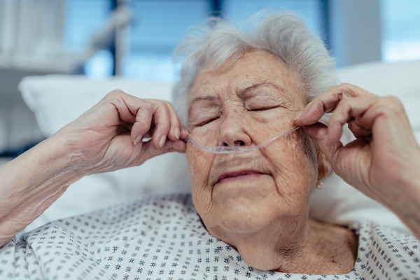 Portrait of senior woman after stroke, heart attack recoverying, lying in hospital bed. Elderly patient in hospital gown with nasal cannula.