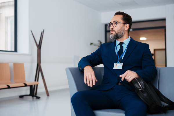 Pharmaceutical sales representative sitting in medical building, waiting for the doctor, presenting new pharmaceutical product. Male drug rep sitting in hall holding smartphone.