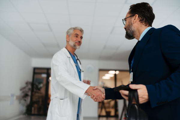 Pharmaceutical sales representative shaking hands with doctor in the medical building. Doctor greeting hospital director, manager in private medical clinic.