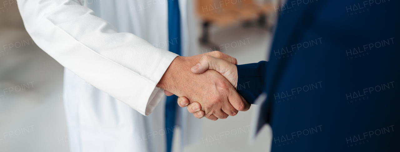 Close up of pharmaceutical sales representative shaking hands with doctor in the medical building. Doctor greeting hospital director, manager in private medical clinic. Banner with copy space.