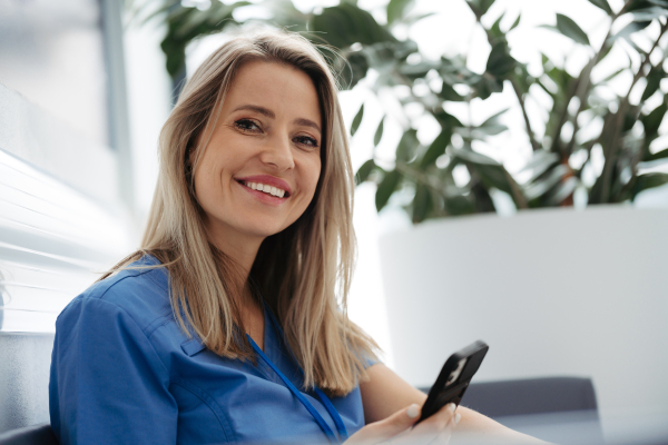 Beautiful female doctor is taking a break during her work shift at hospital, scrolling on smartphone.