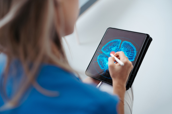 Portrait of female doctor sitting in office, looking at test results, CT scans in tablet. Female surgeon in modern medical clinic using digital technology.