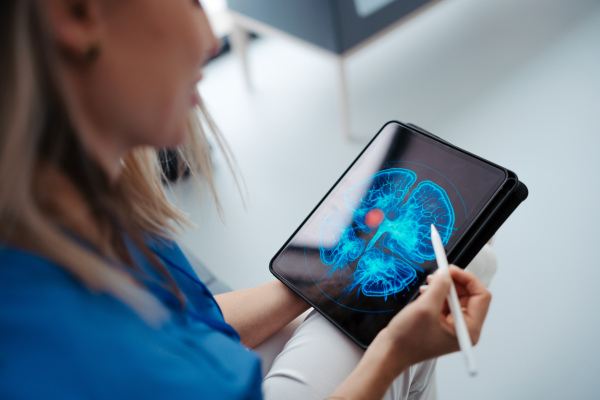 Portrait of female doctor sitting in office, looking at test results, CT scans in tablet. Female surgeon in modern medical clinic using digital technology.