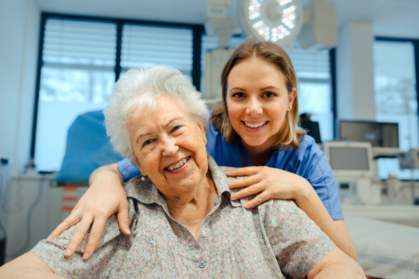 Portrait of caring nurse and senior patient talking in hospital corridor. Emotional support for elderly woman.