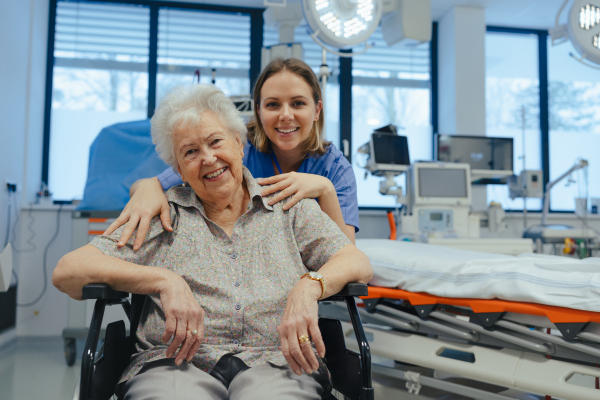 Portrait of caring nurse and senior patient in hospital, looking at camera, smiling. Emotional support for elderly woman.