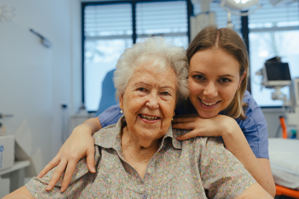 Portrait of caring nurse and senior patient talking in hospital corridor. Emotional support for elderly woman.