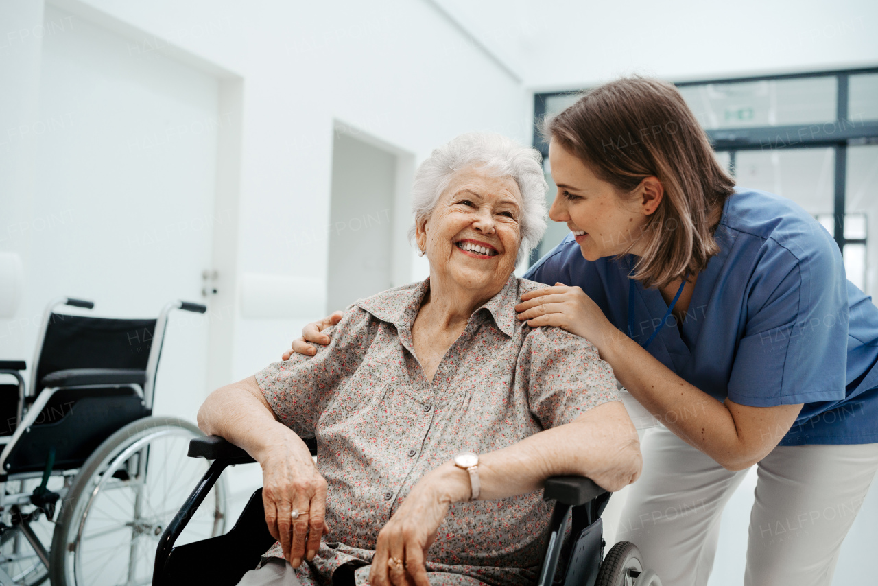 Portrait of caring nurse and senior patient talking in hospital corridor. Emotional support for elderly woman.