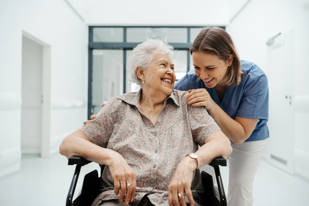 Portrait of caring nurse and senior patient talking in hospital corridor. Emotional support for elderly woman.