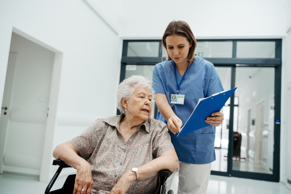 Nurse talking with senior woman, admitting a patient to the hospital, filling documents. Discharging of elderly patient from clinic after surgery.