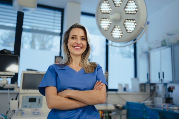 Portrait of ER doctor in hospital working in emergency room. Portrait of the beautiful nurse in blue uniform, crossed arms, smiling.