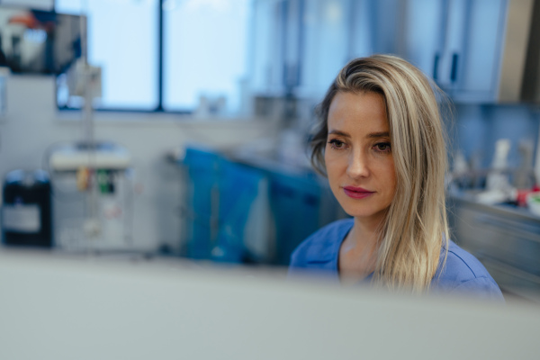 Portrait of ER doctor in hospital working in emergency room. Beautiful nurse in scrubs making call and typing on medical computer in emergency room.