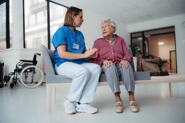 Portrait of caring nurse and senior patient talking in hospital corridor. Emotional support for elderly woman.