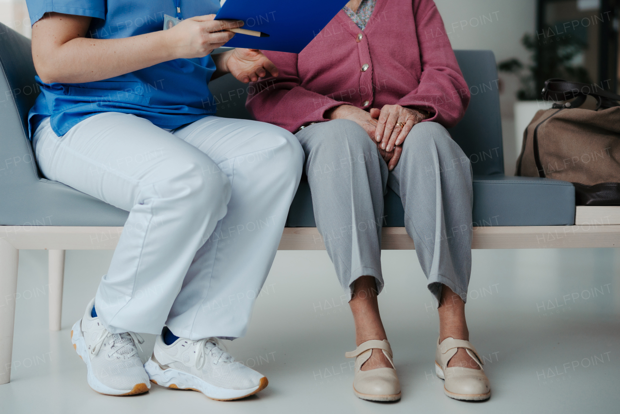 Close up of nurse and senior patient legs, sitting in hospital corridor and talking. Emotional support for elderly woman, concept of geriatrics.