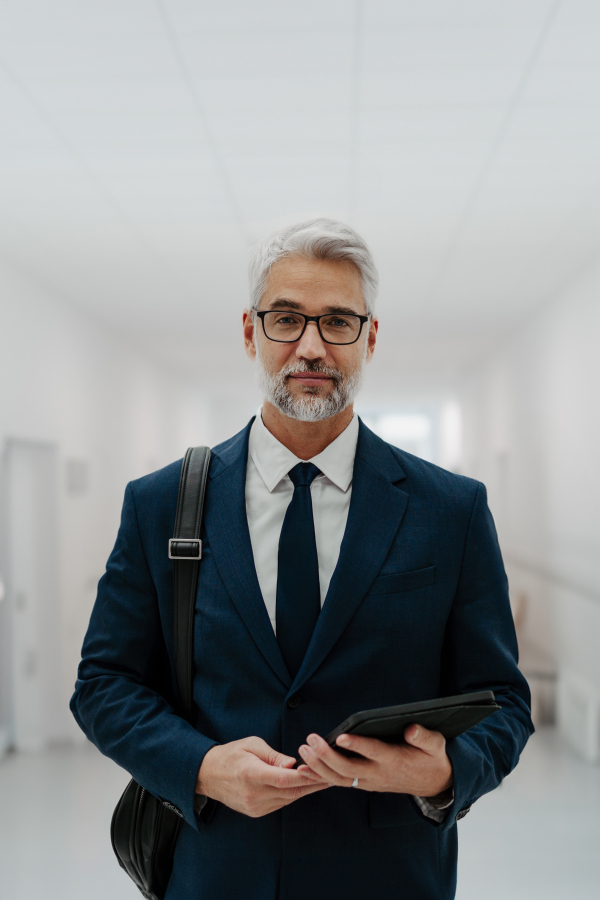 Portrait of pharmaceutical sales representative in medical building, waiting for doctor, presenting new pharmaceutical product. Smiling drug rep standing in hall, modern medical clinic, holding tablet.