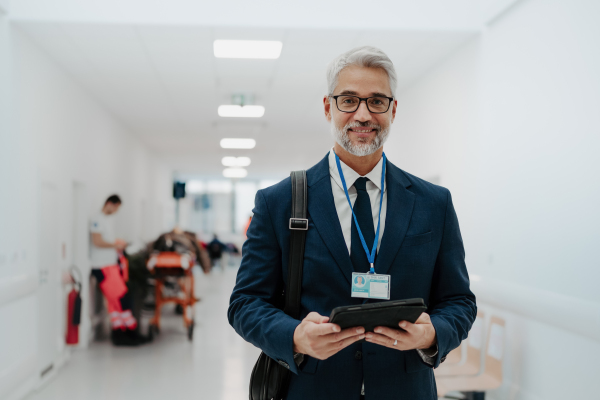 Portrait of pharmaceutical sales representative in medical building, waiting for doctor, presenting new pharmaceutical product. Smiling drug rep standing in hall, modern medical clinic, holding tablet.