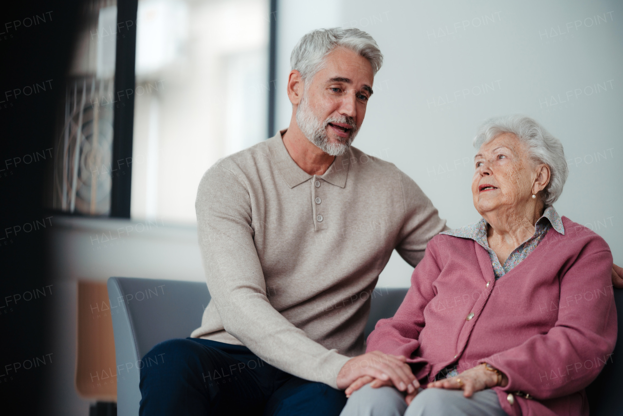 Close up of nurse and senior patient legs, sitting in hospital corridor and talking. Emotional support for elderly woman, concept of geriatrics.