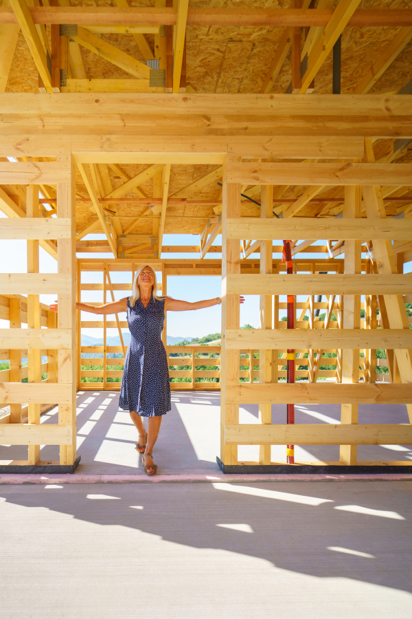 A happy senior woman inside of her new unfinished ecological wooden house.