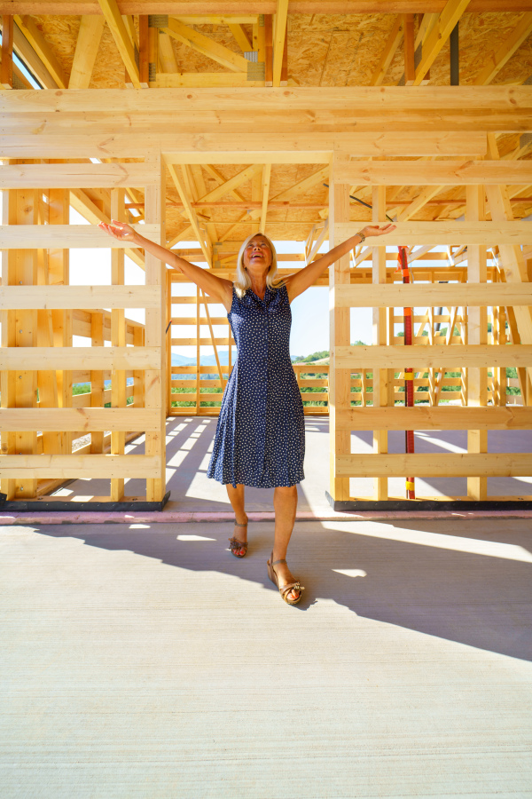 Excited senior woman inside of her unfinished ecological wooden house.