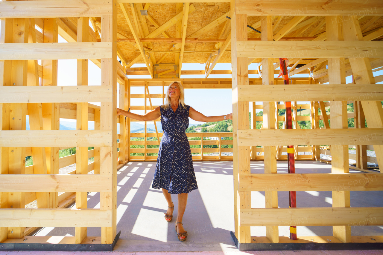 A happy senior woman inside of her new unfinished ecological wooden house.