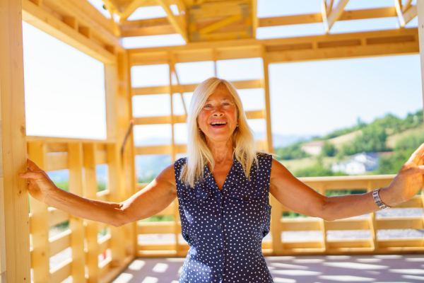 A happy senior woman inside of her new unfinished ecological wooden house.