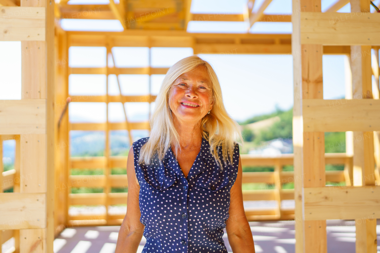 A happy senior woman inside of her new unfinished ecological wooden house.