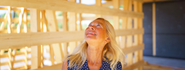 Excited senior woman inside of her unfinished ecological wooden house.