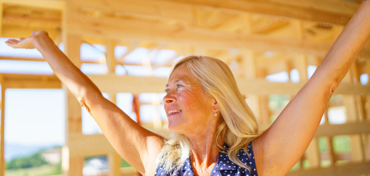 Excited senior woman inside of her unfinished ecological wooden house.