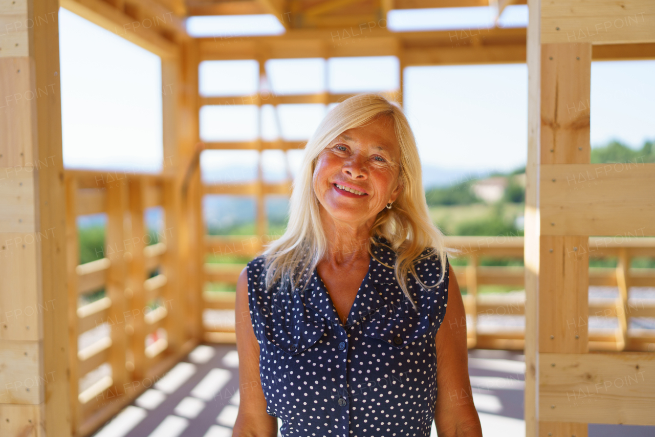 Portrait of happy senior woman inside of her unfinished ecological wooden house.