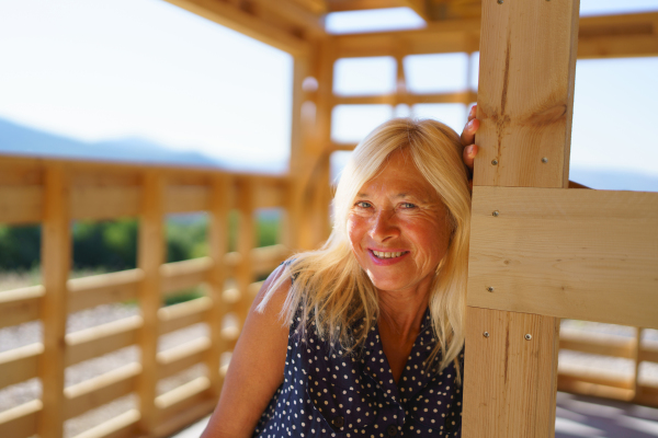 A happy senior woman inside of her new unfinished ecological wooden house.