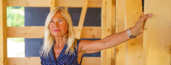 Excited senior woman inside of her unfinished ecological wooden house.