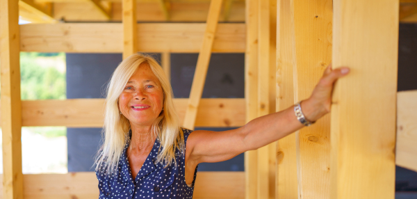 A happy senior woman inside of her new unfinished ecological wooden house.