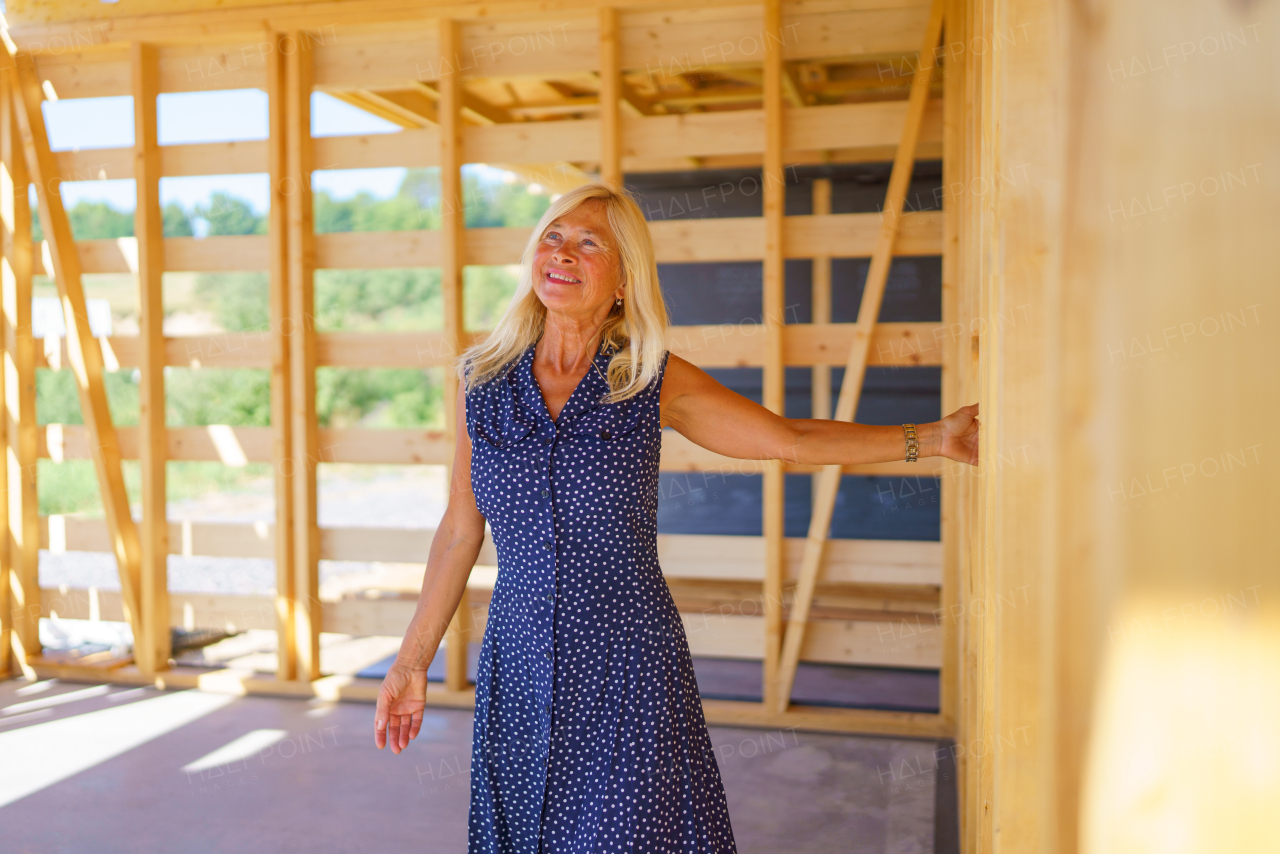 A happy senior woman inside of her new unfinished ecological wooden house.