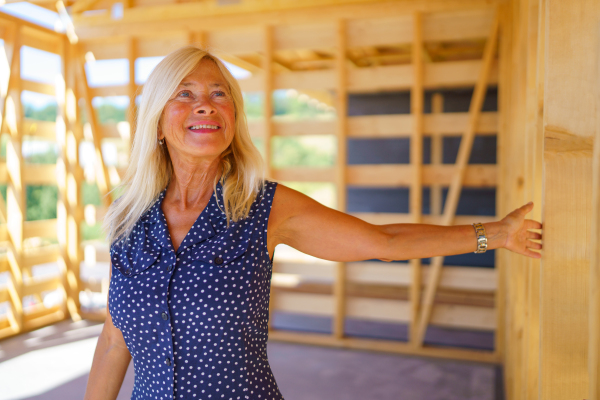 A happy senior woman inside of her new unfinished ecological wooden house.