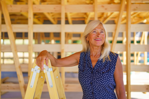 A happy senior woman inside of her new unfinished ecological wooden house.