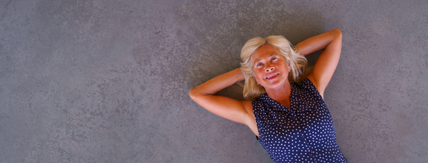 Happy senior woman lying at a concrete floor, wide photography. Copy space.